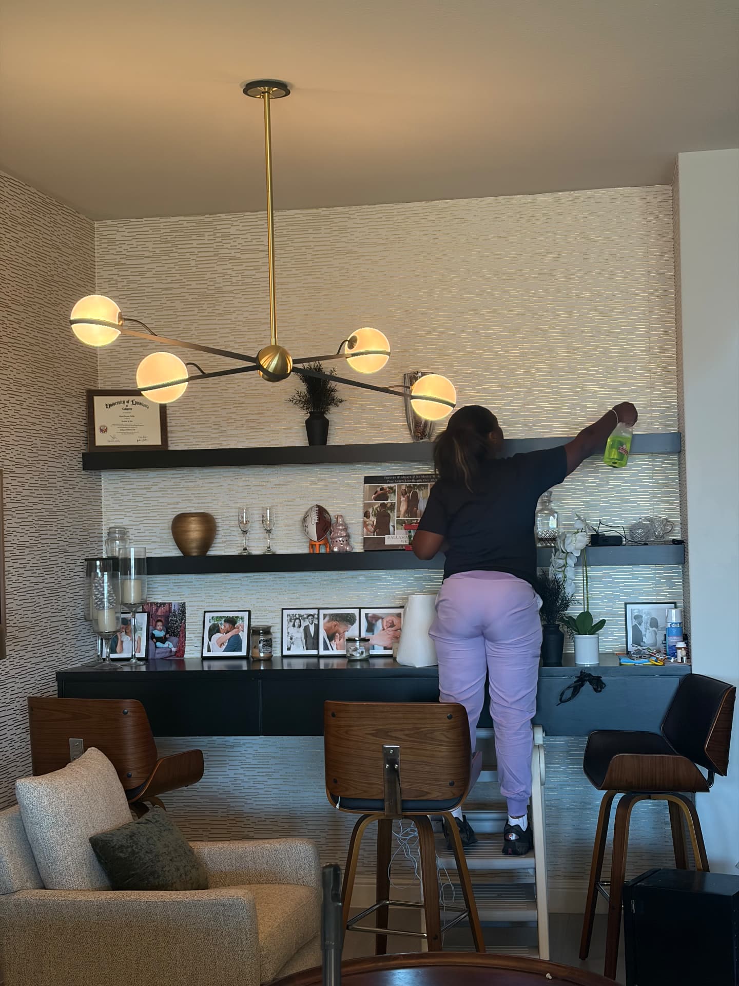 Forever Family cleaner dusting and wiping high shelves in a modern home